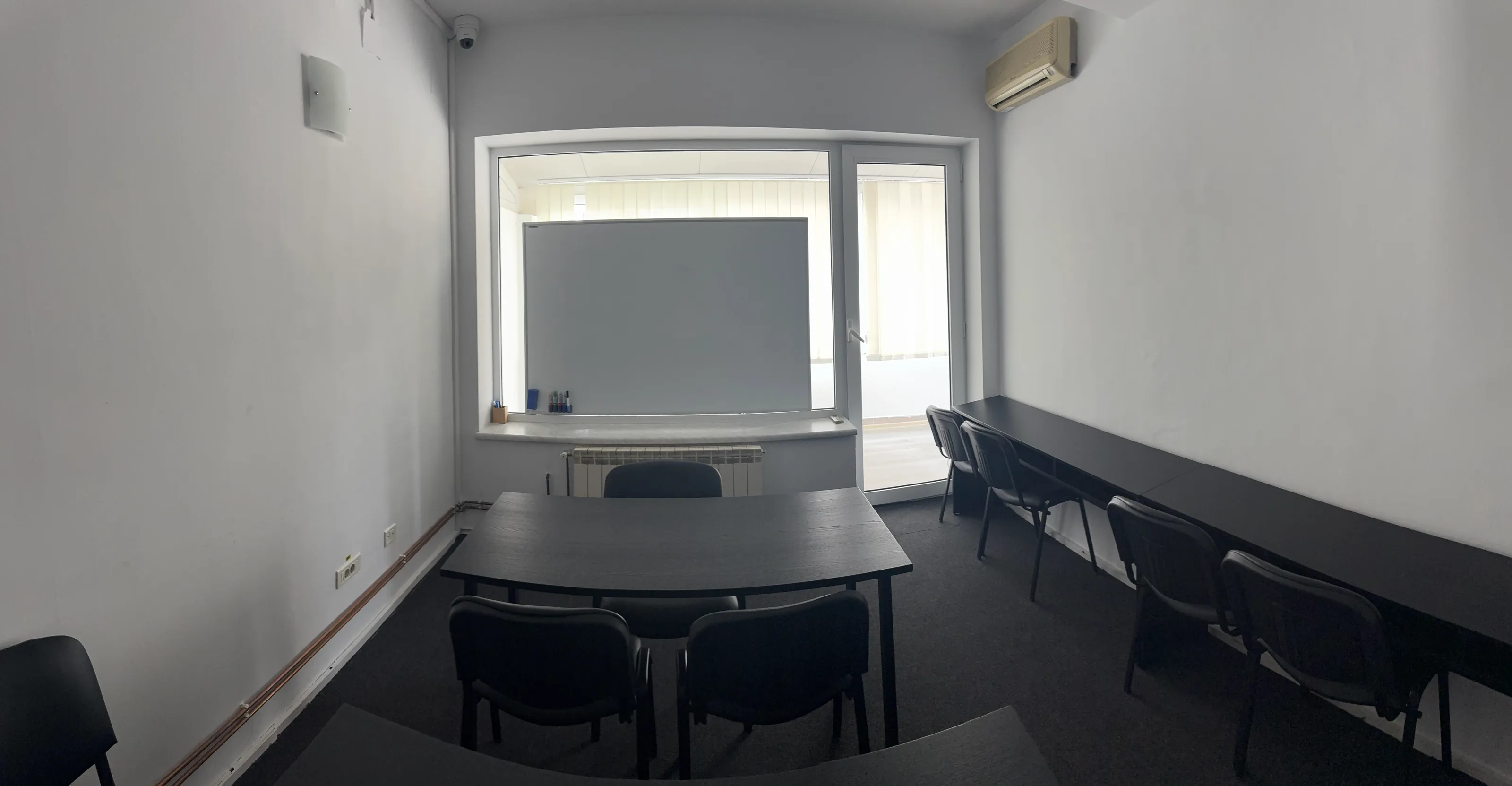 Sala 1 pe toată lățimea: masa centrală cu scaune, tabla albă în fereastră și biroul lung de pe lateral