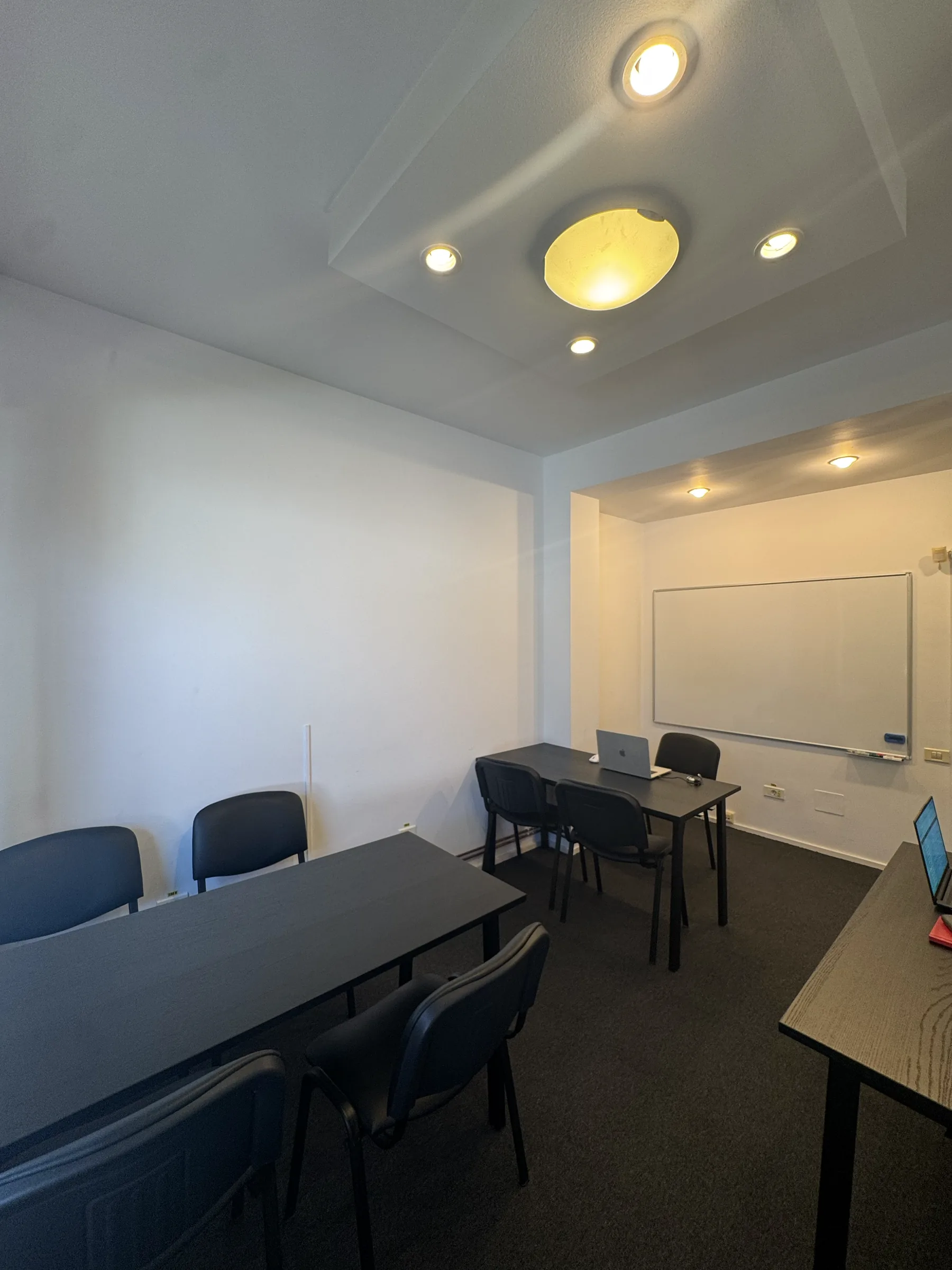 Sala 2 cu tabla albă pe peretele din fund și mesele aranjate în față