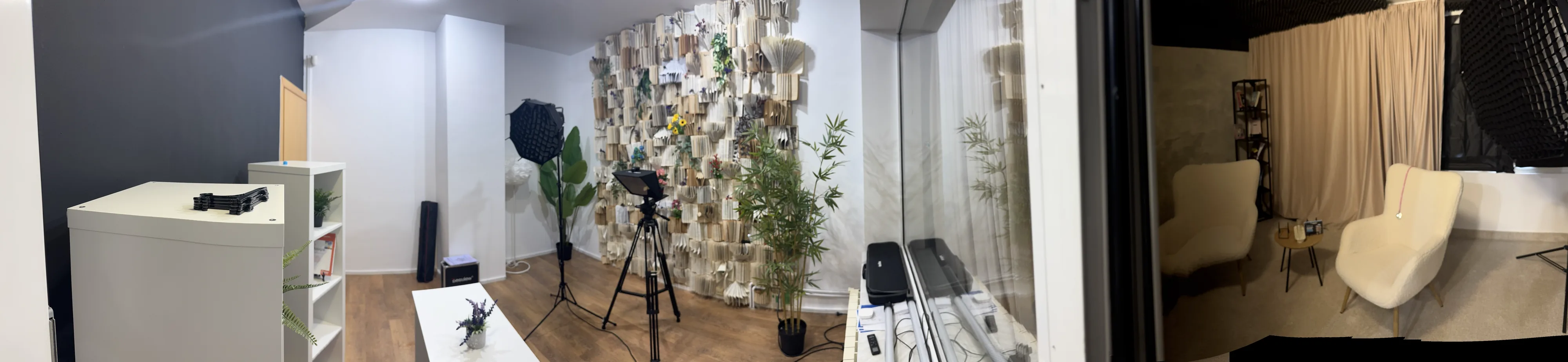 Studioul video pe toată lățimea: masa de prezentare, peretele din pagini de carte cu lumina și camera, și colțul cu fotolii din dreapta